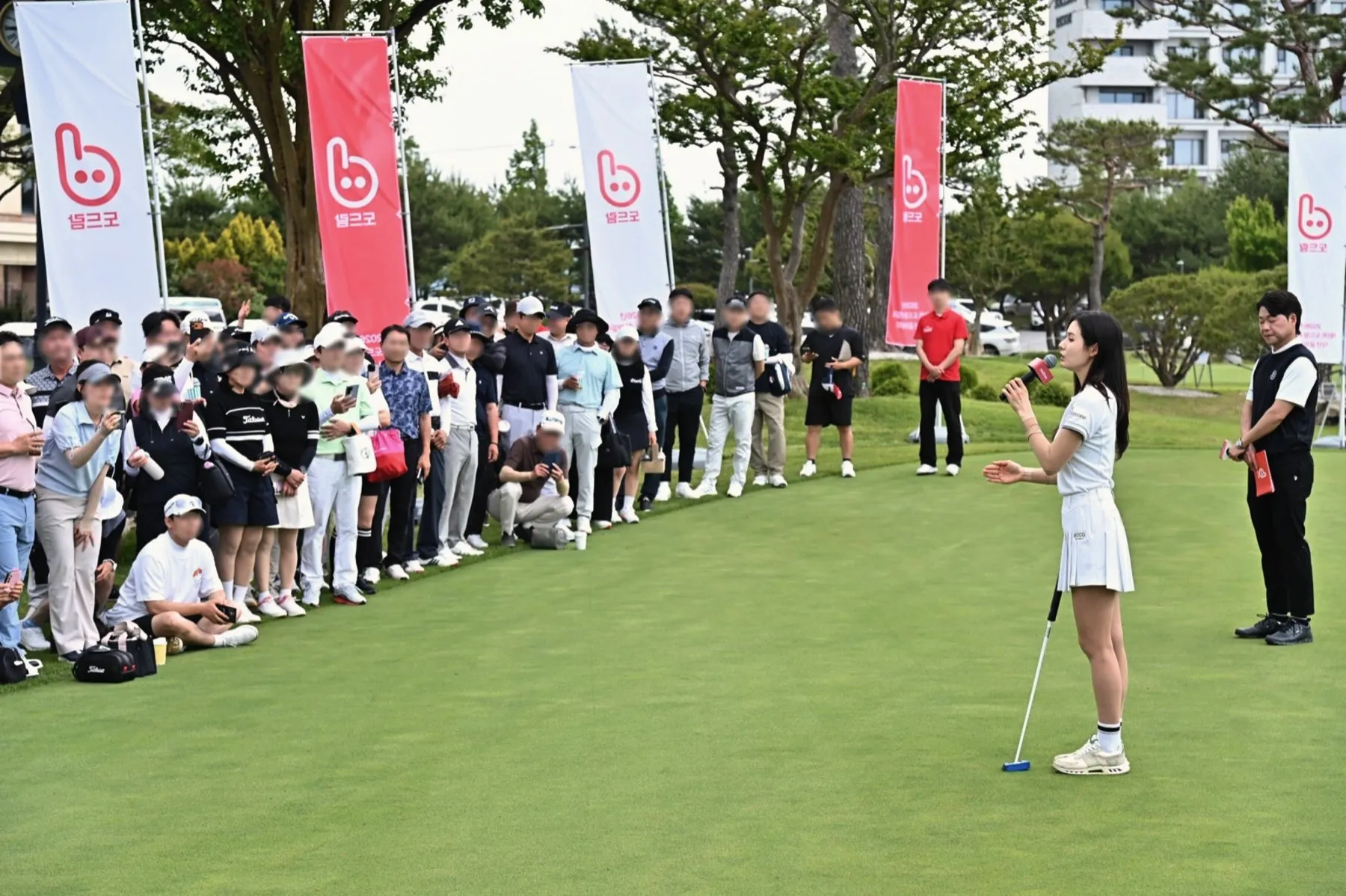 A pro golfer leading a clinic for a crowd of guests on the practice green