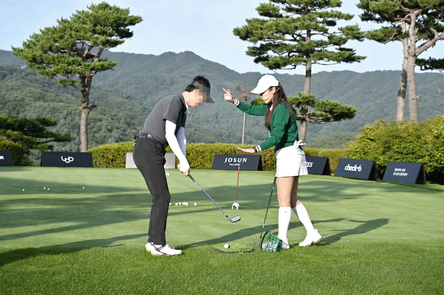 A pro golfer coaching a guest’s swing on the driving range