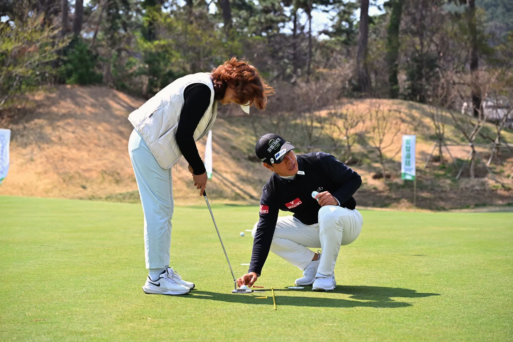 A KPGA pro reading a putt with a guest on the practice green